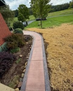 Curved reddish brown concrete sidewalk with a border along a house in Wilson, NC