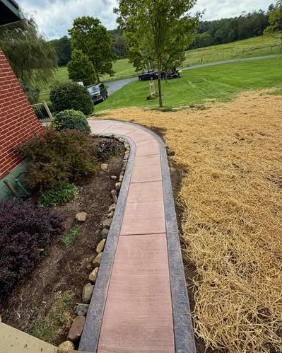 Curved reddish brown concrete sidewalk with a border along a house in Wilson, NC