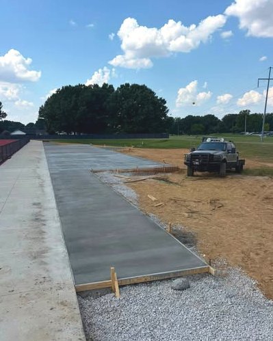 Long concrete sidewalk being poured beside an athletic field with a concrete truck in Wilson, NC