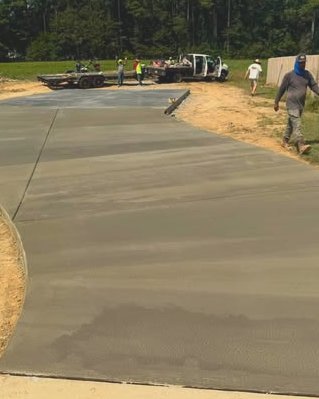 Long gray concrete driveway being finished by a crew with trucks nearby in Wilson, NC